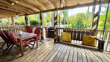 Eine Holzterrasse mit Tisch, Stühlen, einer Schaukel und einem Grillbereich.