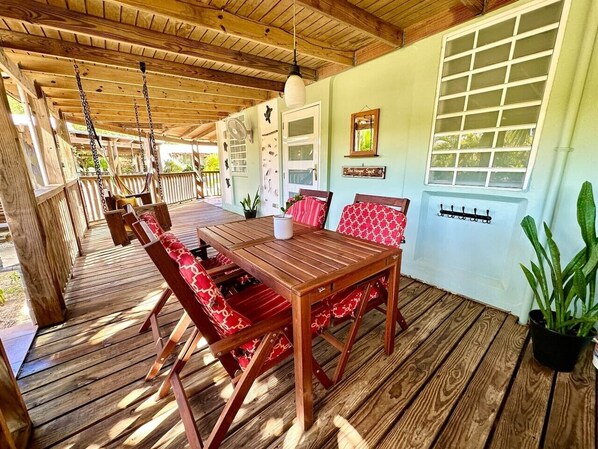 An outdoor wooden deck with a table and chairs, a hanging light fixture, and a window with a view.