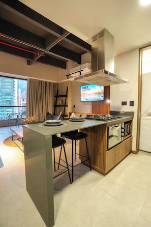 Una cocina moderna con una isla central, taburetes de bar, horno empotrado y un televisor mostrando 'DEEP HOUSE' en la pared.