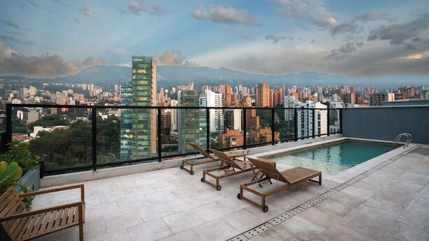 A rooftop pool with lounge chairs, a cityscape view, and a modern building in the background. - Apartamento Mixa (Medellín)