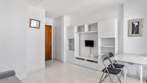 Una habitación con un escritorio blanco, un televisor montado en la pared y una puerta que da a otra estancia.