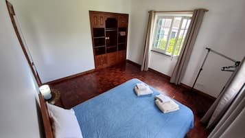 A bedroom with a bed, wooden wardrobe, and a window with curtains.