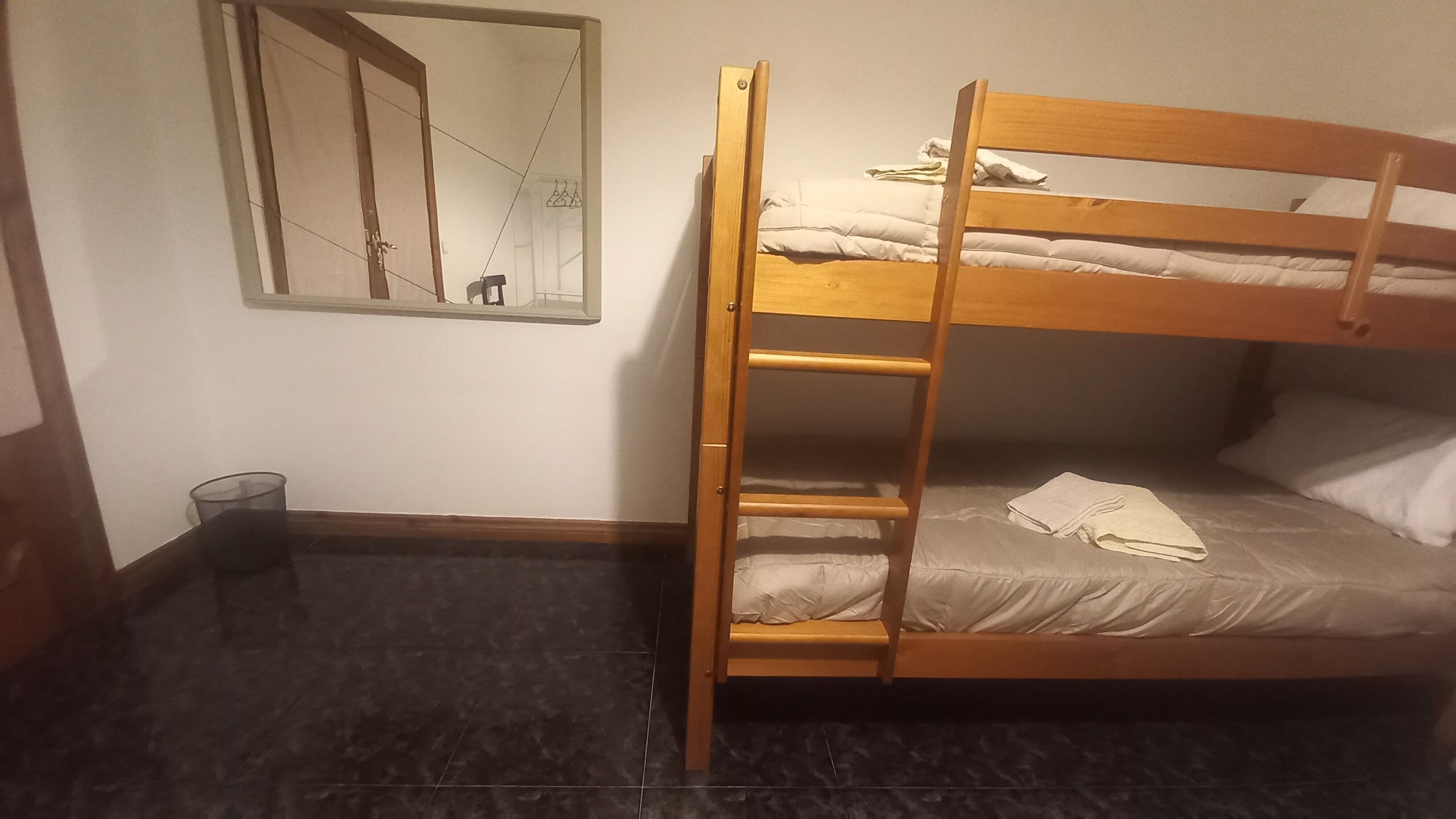 A bunk bed with a ladder, a mirror on the wall, and a small trash bin.