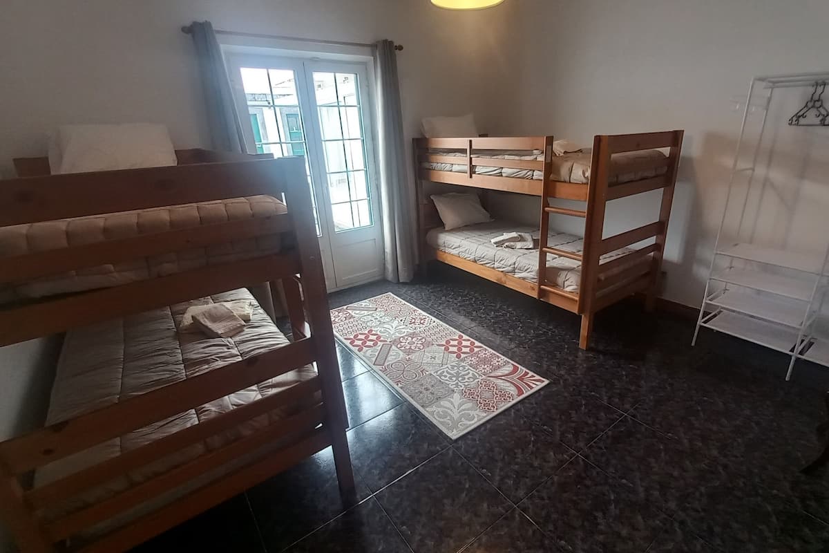 Una habitació amb tres llits superposats, un moqueta amb dibuixos i una paret blanca amb una estant per a la roba.