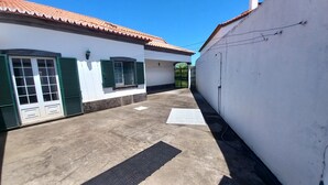 Un callejón estrecho con un edificio blanco que tiene persianas verdes, techo de baldosas y suelo de hormigón.