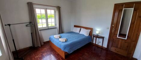 Une chambre avec un lit en bois, une table de chevet avec une lampe, une fenêtre avec des rideaux et un plancher en bois.