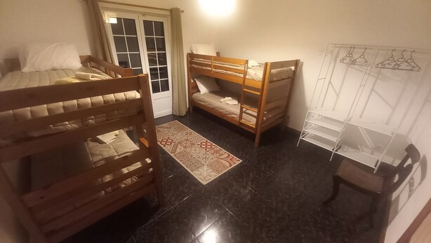 Una habitación con dos literas, un escritorio pequeño, una silla, un armario con espejo y una alfombra estampada.