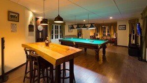 A pool table in a room with a wooden table and bar stools, a ceiling with a grid pattern, and a television on the right.