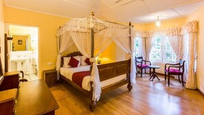 A four-poster bed with a canopy, a small table with chairs, a ceiling fan, and a window with curtains.
