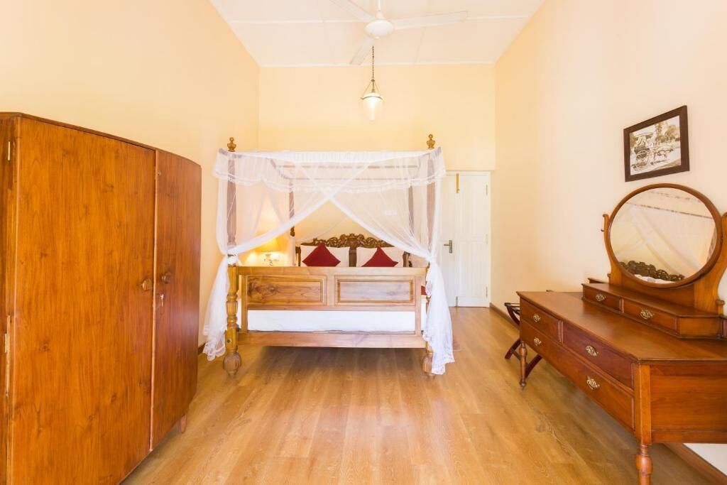 Una camera da letto con un letto in legno, un comodino, una cassettiera, uno specchio e una ventola a soffitto.
