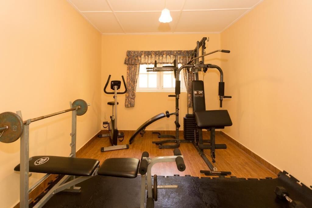 Un gimnasio con equipo de levantamiento de pesas, bancos y una ventana con cortinas.