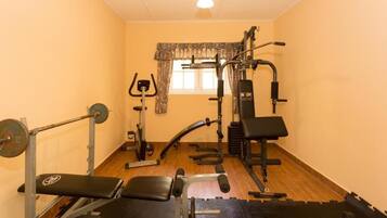 Un gimnasio con equipo de levantamiento de pesas, bancos y una ventana con cortinas.
