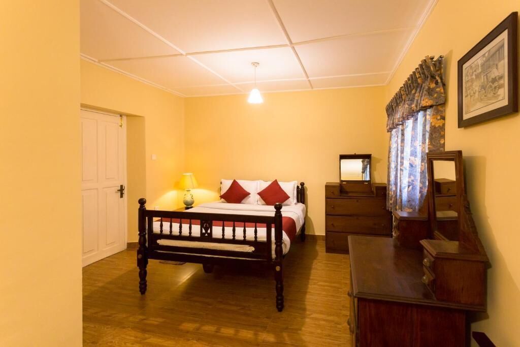 A bedroom with a wooden bed, a bedside table, a dresser, a lamp, and a mirror.