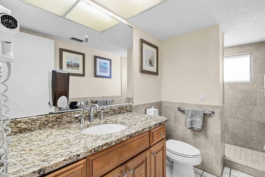 A bathroom with a granite countertop sink, a large mirror, a toilet, and a shower area.