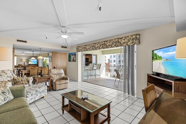 A spacious living room with a large flat-screen TV, a ceiling fan, and a view to the outside. - Calini Beach Club by Coolvacay (Siesta Key)