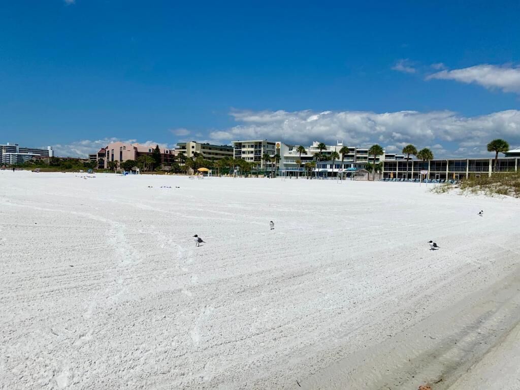 Een strand met een uitgestrekt zandgebied, gebouwen op de achtergrond en een heldere lucht.