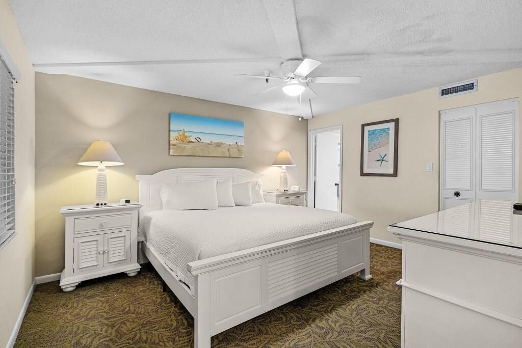A bedroom with a bed, two bedside tables, a ceiling fan, and a painting on the wall.