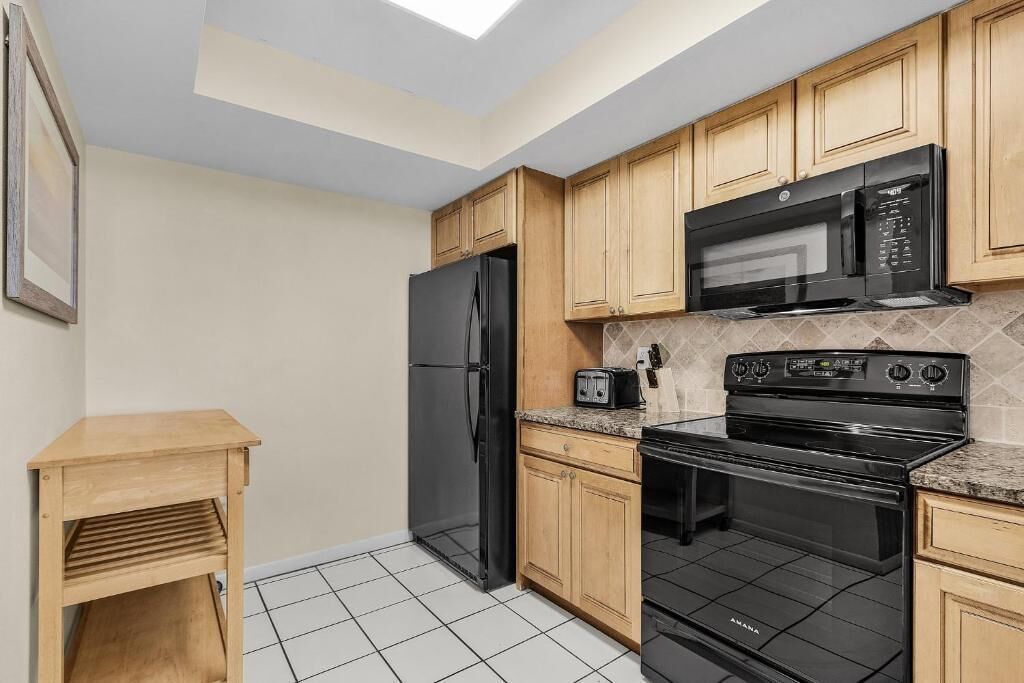 A compact kitchen with wooden cabinets, a black refrigerator, a microwave, a toaster, and a black stove.
