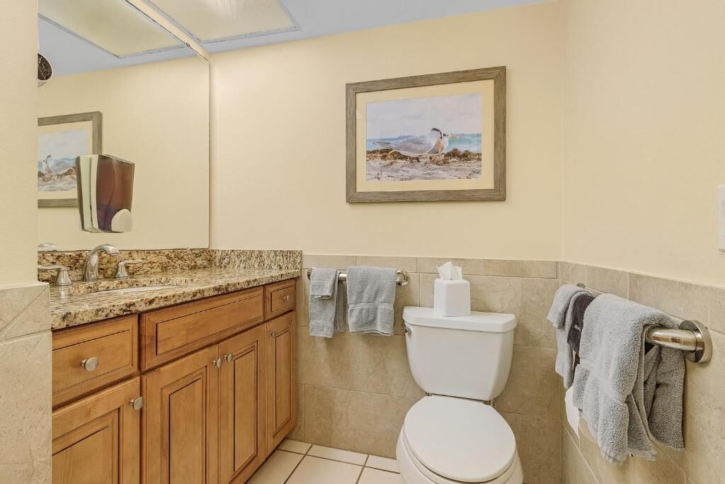 A bathroom with a toilet, sink, wooden cabinets, and a framed picture on the wall.