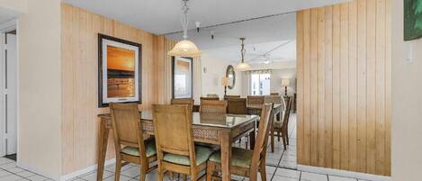A dining area with a wooden table and chairs, a framed picture on the wall, and a ceiling fan.