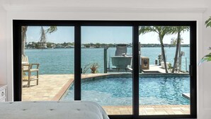 Ein Schlafzimmer mit einer großen Schiebeglasdoor zum Poolbereich mit Blick auf das Wasser und Palmen.