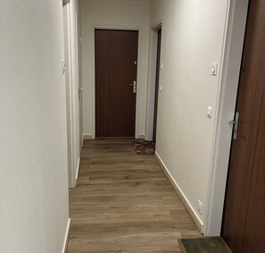 Ein Flur mit Holzboden, weißen Wänden und einer verschlossenen Tür am Ende.