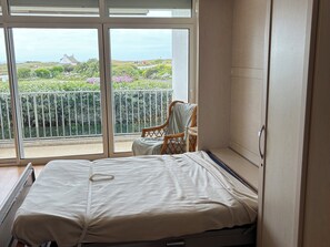 Ein Zimmer mit einem Bett, einem Sessel und Blick auf einen Balkon mit Grünpflanzen und ein Gebäude in der Ferne.
