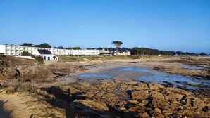 A coastal area with rocky terrain, a white building with blue doors, and a tree in the background. - Grand studio Résidence les 3 Iles Quiberon N°28 (Quiberon)