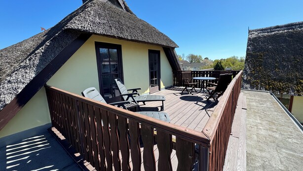 Een gebouw met rieten dak, een houten terras, zitplaatsen buiten en uitzicht op de omgeving.