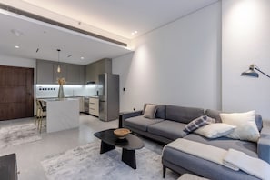 A modern living room with a grey sofa, a coffee table, and a kitchen area in the background. - Modern 1B | Rooftop Pool | DIFC and DowntownAccess (Dubai)
