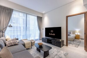 A modern living room with a sofa, TV, and a large window. - Modern 1B | Rooftop Pool | DIFC and DowntownAccess (Dubai)