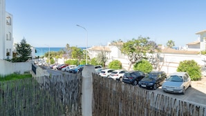 A coastal residential area with parked cars, a wooden fence, and buildings with balconies.