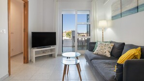A living room with a television, a sofa, a glass coffee table, and a view through a glass door.