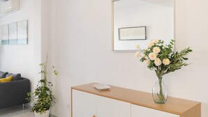 A modern room with a wooden console table, a vase with flowers, a grey sofa, and a large mirror on the wall.