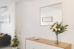 Ein modernes Zimmer mit einem Holztischchen, einer Blumenvase, einem grauen Sofa und einem großen Spiegel an der Wand.