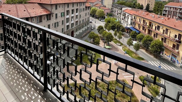 A balcony with a metal railing overlooking a cityscape with buildings, trees, and a clear sky. - Spacious Living with Balcony near Fondazione P... (Milan)