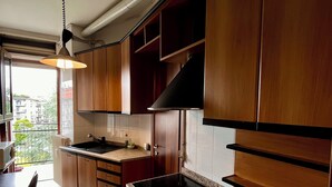 A kitchen with wooden cabinets, a granite countertop, a stove, and a window with a view of buildings. - Spacious Living with Balcony near Fondazione P... (Milan)