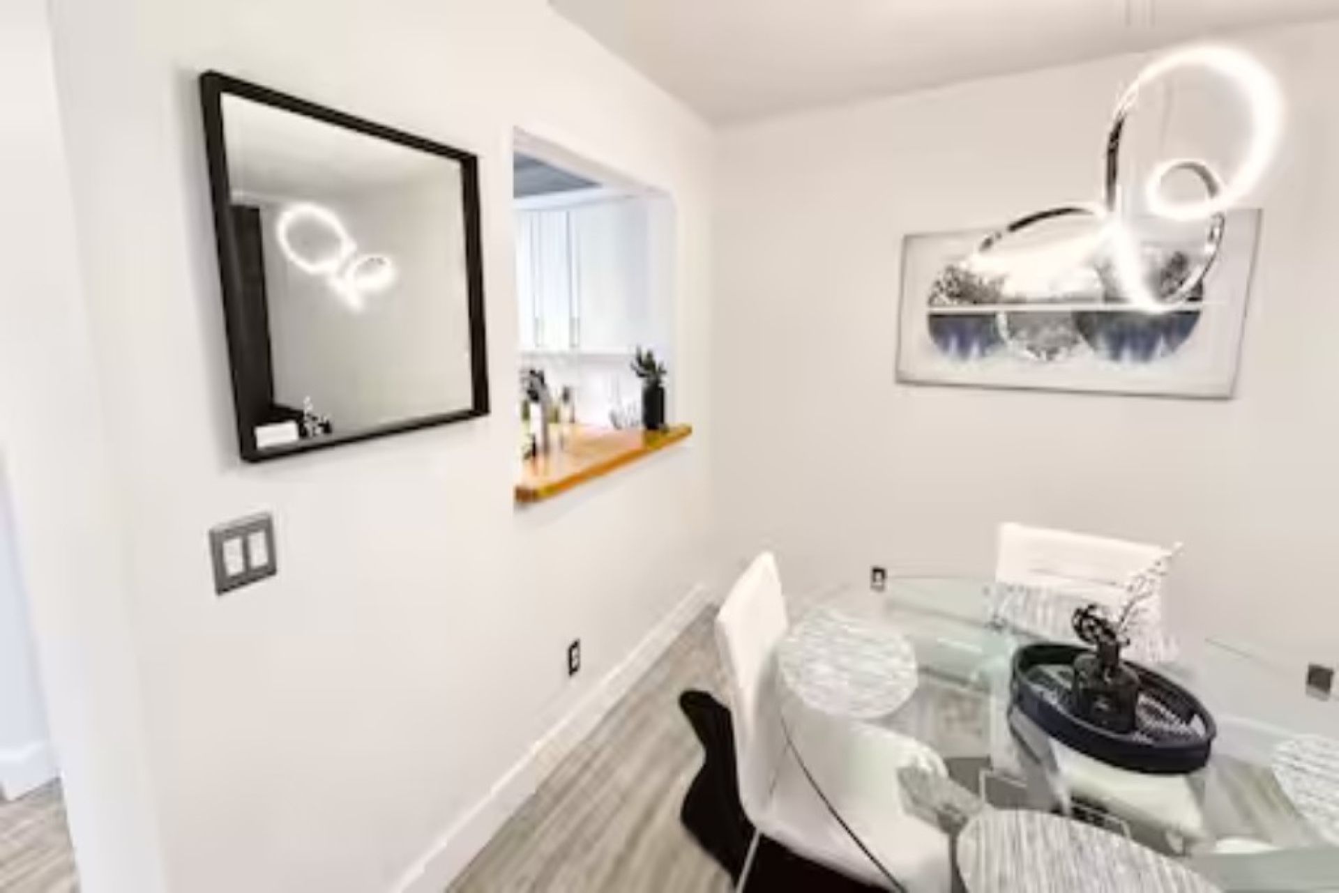 A modern dining area with a glass table, chairs, and a wall-mounted mirror.