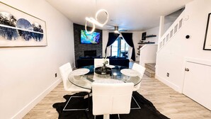 A modern dining area with a glass table, white chairs, a fireplace, and a TV mounted on the wall. - Lakefront |Long Term Friendly |Pets|Cozy Fireplace (Jacksonville)
