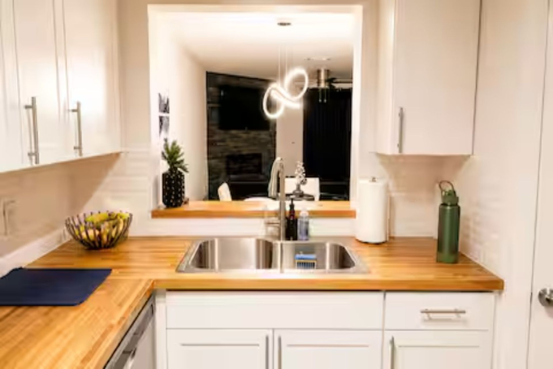 Une cuisine moderne avec un plan de travail en bois, un évier en acier inoxydable et des armoires blanches.