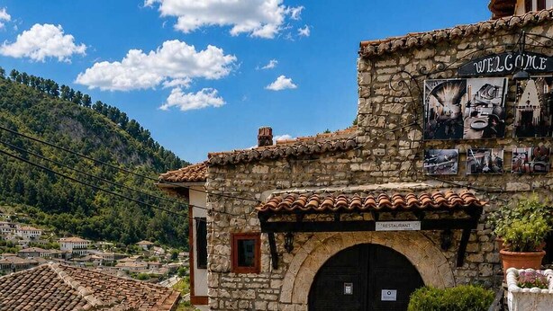 A stone building with a tiled roof, a black door, and a sign that reads 'Welcome.' - Guva Stone House Mangalem (Berat)