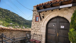 A stone building with a dark wooden door, a sign indicating a private house, and a terrace with a metal railing and red cushions. - Guva Stone House Mangalem (Berat)