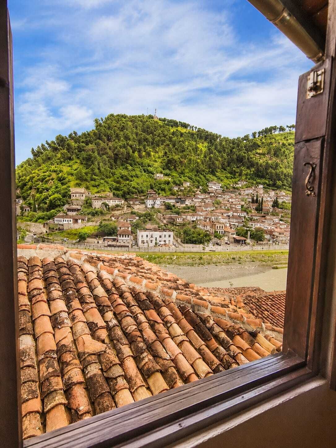 A view from a window overlooking a hillside village with terracotta roofs and traditional buildings.