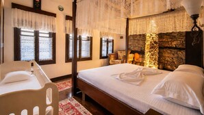 A bedroom with a four-poster bed, lace curtains, a stone fireplace, and a red patterned rug. - Guva Stone House Mangalem (Berat)