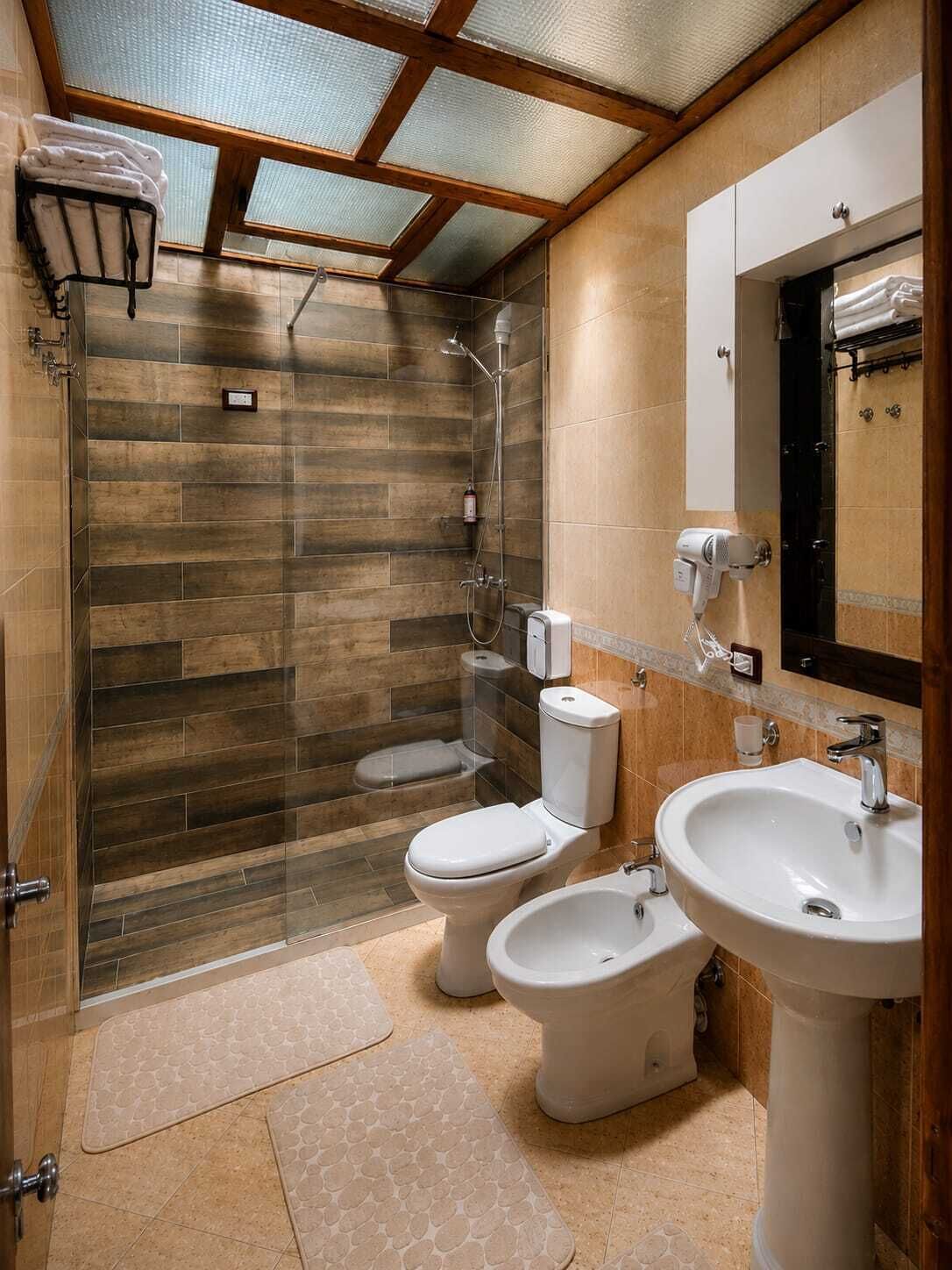 Une salle de bain avec une douche, deux toilettes, un lavabo et un miroir.