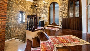 A stone-walled room with wooden beams, a bench, a rug, and a wooden door with glass panels. - Guva Stone House Mangalem (Berat)