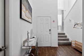 A hallway with a white door, a staircase, and a wall-mounted artwork. - Spacious Retreat | Pool Table, Firepit + Backyard (Houston)