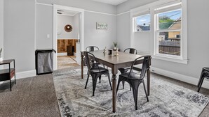 A dining area with a table and chairs, a rug, a trash can, and a window with a view. - Renovated / Fully Stocked Kitchen / Queen Bed (Bay City)