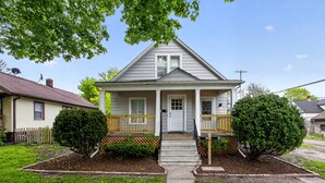A two-story house with a front porch, a small front yard, and a driveway leading to the entrance. - Renovated / Fully Stocked Kitchen / Queen Bed (Bay City)