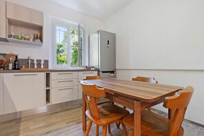 Una cucina moderna con mobili in legno, un frigorifero in acciaio inossidabile, un tavolo da pranzo in legno con sedie e una finestra vista su un’area verde.